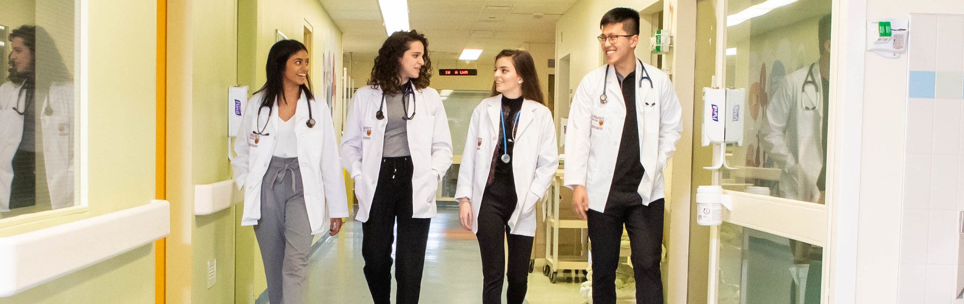 Four students dressed in white coats in a hallway